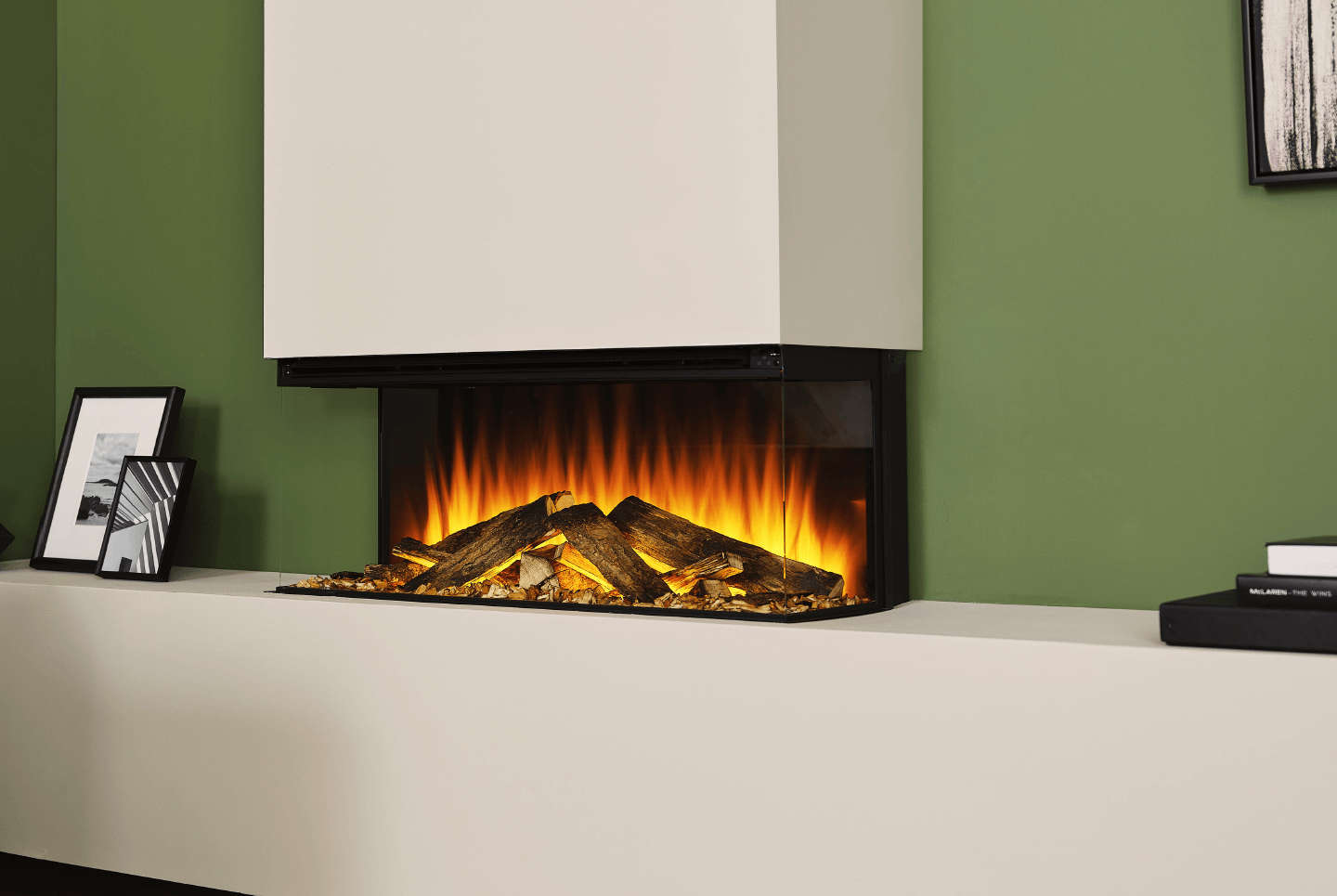 Modern fireplace with glowing flames and decorative logs against a green wall.